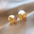 Primer plano de elegantes pendientes de mariposa bañados en oro con cierres de perlas grandes - Pendientes de Botón Mariposa