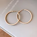 Detailed close-up showing the texture of beige leather wrapped golden hoop earrings - Brown