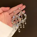 Close-up of elegant floral crystal tassel earrings with AB rhinestones held in hand. - Large Hoop Crystal Tassel Style (27) / Silver