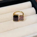 Gros plan d'une élégante bague ouverte dorée avec pierres carrées violettes et roses - Or