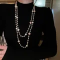 Detailansicht einer langen zweireihigen Perlenkette mit Kleemotiven auf einem schwarzen Pullover - Vierblättriges Kleeblatt Anhänger (Item 3)