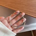 Macro view of large silver-toned minimalist hoop earrings held in hand for detail - Style 11 / Diameter 60mm / Silver