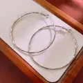Detailed close-up of textured silver hoop earrings presented on a minimalist wooden tray - Hammered Hoop (HE8275) / 59mm / Silver