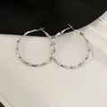 Detailed close-up of large silver-toned twisted hoop earrings on a neutral background. - Style 50 / Silver