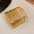 Detailed macro shot of a gold multi-strand wire wrap wide cuff bracelet on a white surface. - Multi-layer / Gold