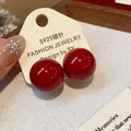 Primo piano di orecchini a bottone tondi rossi lucidi su cartoncino con perni in argento S925. - Medio (2cm) / Rosso