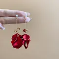 Elegant long drop earrings with deep red petal tassels and gold accents held by a hand. - 106# Dark Red Petal Long Tassel Style / Red