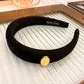 Close-up of the elegant gold oval metal ornament on a black padded sponge headband - Oval (HH3763) / Black