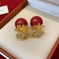 Close-up of red pearl earrings with golden firework rhinestone design in a gift box. - Red