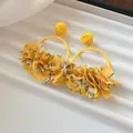 Close-up detail of stylish yellow fabric petal hoop earrings for early spring beach look - Yellow