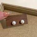 Close-up detail of elegant round white iridescent pearl stud earrings displayed on a wooden board - Imitation Shell Pearl (HE8071) / 12mm Strand