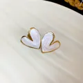 Macro view of elegant gold heart-shaped stud earrings with white pearly enamel - White