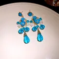 Dettaglio ravvicinato di orecchini pendenti con fiori blu e cristalli dorati - Perno in argento - Oro - Blu