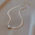 Elegant gold leaf-link necklace with white pearls displayed on soft beige fabric background - Wheat Ear
