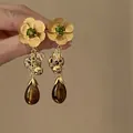 Detail shot of pleated metal flower earrings with green gemstone and tassel charms - Emerald Tassel Style / Rhinestone Inlaid / Gold