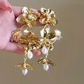 A detailed macro view of stylish gold-tone metallic flower dangle earrings with pearls - Floral Pearl Tassel Style / Pearl Decoration / Gold