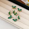 Detailed view of green zircon butterfly tassel earrings on a velvet jewelry tray. - Gold-Green