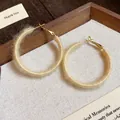 Close-up of beige fabric-wrapped hoop earrings on a textured fabric background. - White