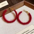 Detailed macro view of red fabric woven hoop earrings with golden clasps on warm fabric. - Red