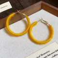 Detailed macro view of yellow yarn-wrapped hoop earrings on textured wooden display tray - Yellow