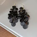 Detailed close-up of black shell disc tassel earrings with shiny fish scale design - Black