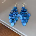 Close-up of bohemian blue shell disc tassel earrings on a minimalist grey background - Sapphire Blue