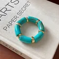 Detail view of a turquoise marbled cylinder bead bracelet with gold spacers on a book. - Cylindrical Smudge Style (HB3370) / Gold-Green