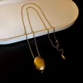 Detailed view of a gold titanium steel necklace with an oval pendant on a white tray - Oval Pendant Style / Gold