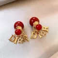 Primo piano di orecchini a perla rossa con ciondoli D-I-R dorati e dettaglio stella - Stile Ciondolo Lettere DIR (11#)