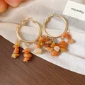 Close-up of gold hoop earrings featuring irregular orange natural stone tassels. - Gold - Silver Post / Orange