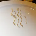 Close-up of elegant gold wavy long tassel drop earrings displayed on a white plate - Wave (10#)
