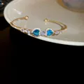 Elegant gold-plated adjustable bangle featuring twin blue heart-shaped zircons and crystals. - Style 50 / Gold-Blue