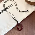 Detail of a dark red irregular oval pendant necklace on a minimalist canvas background - Red