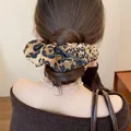 Close-up of leopard print pleated scrunchie with black bow on a low bun hairstyle. - Coffee Leopard