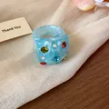 Detailed close-up of a light blue chunky resin ring with colorful rhinestone inlay. - Cyan