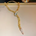 Detail view of golden snake chain necklace with sparkling rhinestones and green eyes. - Gold