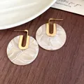 Primo piano di orecchini circolari in acetato con trama marmorizzata e dettagli dorati - Motivo Marmo Rotondo / Perno in argento 925 / Bianco Crema