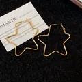 Vista detallada de los pendientes de aro dorados con forma de estrella en fondo negro - Dorado