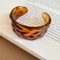 Macro view of a tortoiseshell resin cuff bracelet with a rippled wavy texture detail - Amber