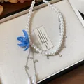 Close-up of blue beaded flower and teardrop pearl pendant on a white pearl necklace - Blue
