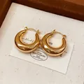 Nahaufnahme von klobigen 18 Karat vergoldeten Creolen auf einer strukturierten Karte - Gold