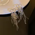 Macro view of sparkling heart-shaped rhinestone tassel earrings on a dark surface. - Heart Style / 925 Silver Needle / Silver