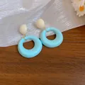 Primo piano di orecchini a cerchio in acrilico azzurro con perni bianco crema su legno - Blu