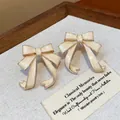 Detailed view of cream enamel bow stud earrings on a vintage textured background - Beige Enamel Bowknot