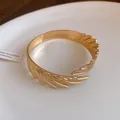 Detailed macro view of the intricate gold feather texture on the open metal bangle. - Feather Style / Gold