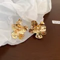 Detail view of gold-tone crinkled petal-shaped earrings on white paper texture - Flower Style (HE3125)