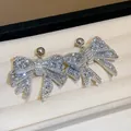 Detailed macro view of silver needle bow earrings encrusted with sparkling rhinestones. - White