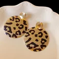 Primo piano di eleganti orecchini leopardati dorati su un vassoio di ceramica bianca. - 55# Bottone in Oro Martellato / Oro Nero