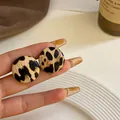 Primer plano de modernos pendientes redondos con estampado de leopardo sostenidos a mano - Estilo Botón Redondo (1#) / Leopardo Redondo