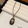 Détail macro du pendentif en pierre oeil de tigre dans un cadre ovale en résine sur cordon brun - Design Ovale / Café